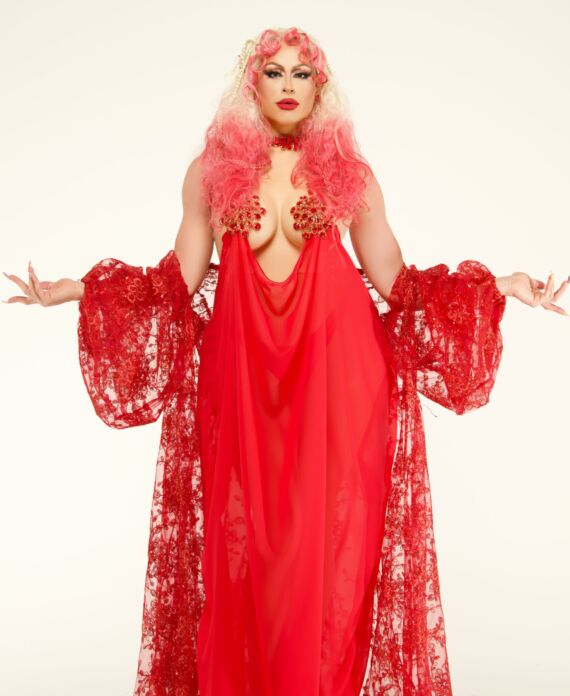 Drag performer in a flowing red gown with lace details and pink-blonde hair for Palace South Beach in Miami Beach