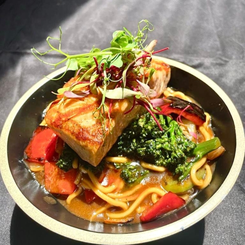 Grilled salmon served over noodles and vegetables, Asian-inspired cuisine