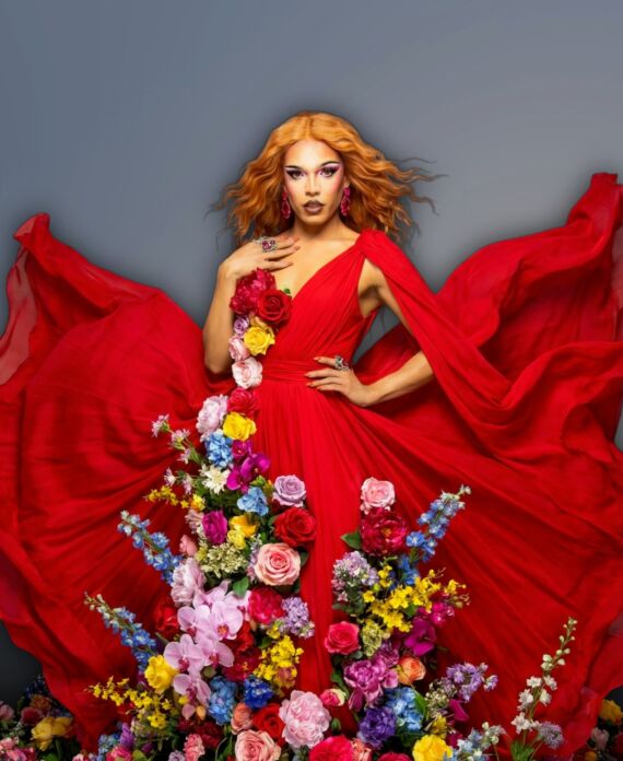 D'Vice Dion in a flowing red gown surrounded by colorful flowers for Palace South Beach in Miami Beach