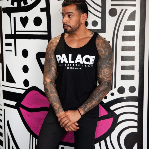 Two men wearing matching pink Palace South Beach tank tops in front of the drag bar’s storefront