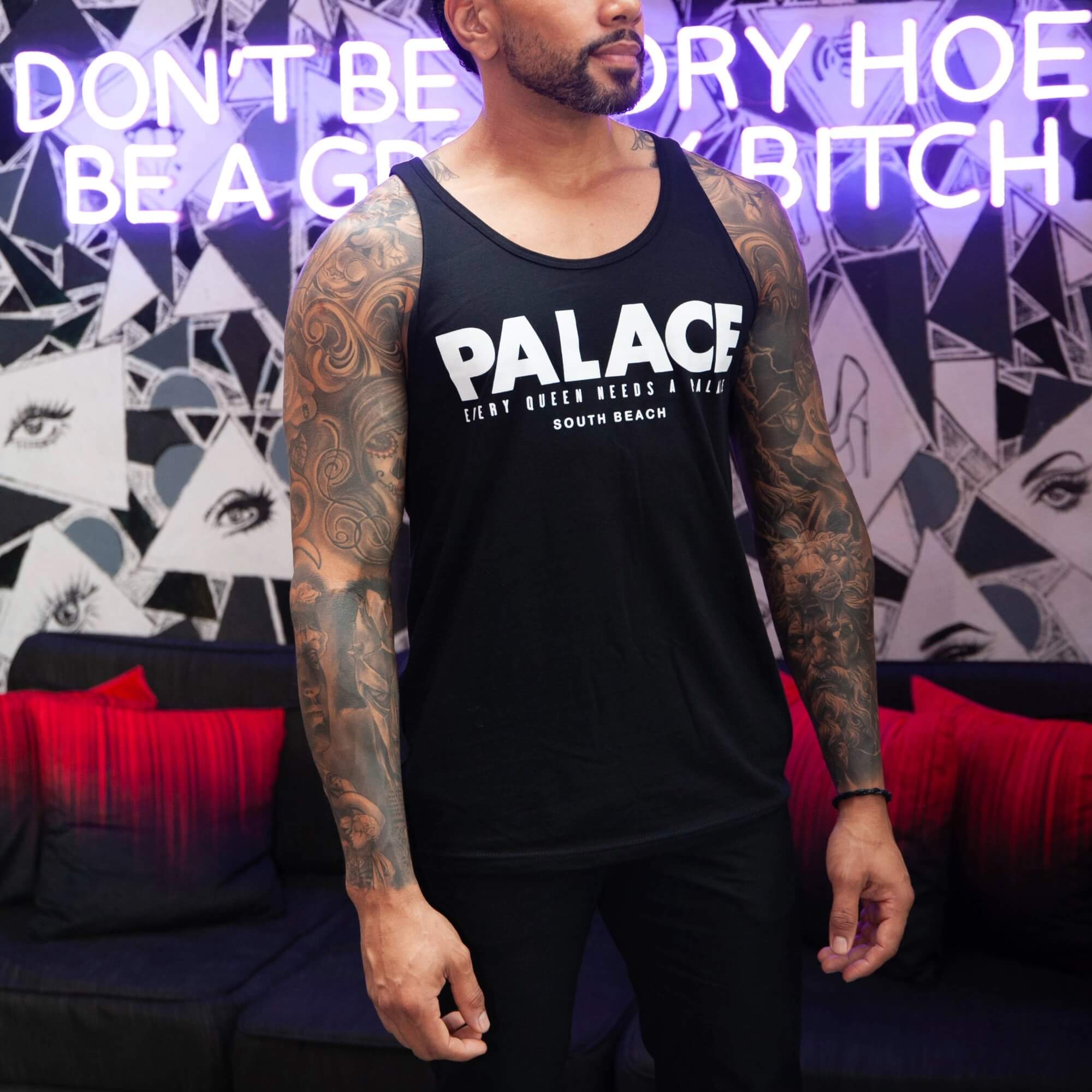 Pink Palace South Beach Tank Tops – LGBTQ+ Summer Style Two men wearing matching pink Palace South Beach tank tops in front of the drag bar’s storefront